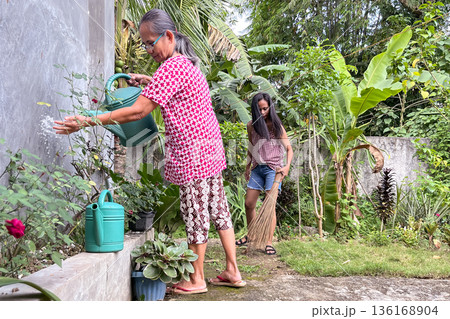 An elderly Asian woman and her daughter clean up their yard in the Philippines 136168904