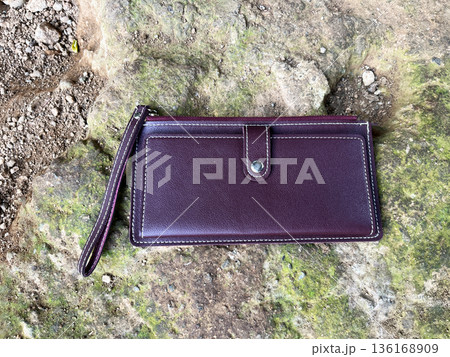 burgundy leather wallet with wrist strap lost in wild mossy rocks 136168909