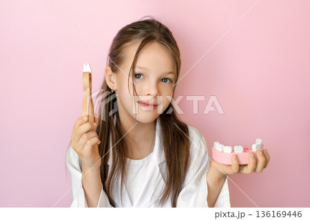 Child with dental tool and jaw model symbolizing first milk tooth loss, pediatric dentistry care, oral health prevention, and professional dental clinic services for World Oral Health Day. 136169446