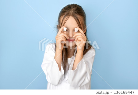 Smiling child holding milk teeth near eyes symbolizing first tooth loss, childhood dental development, oral hygiene education, and awareness campaign for World Oral Health Day. 136169447