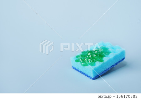 Blue cleaning sponge soaking green dishwashing liquid on blue background Blue cleaning sponge soaking green dishwashing liquid on blue background 136170585