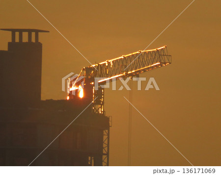 Building tower crane illuminated by golden sunlight at sunset. Urban photo Building tower crane illuminated by golden sunlight at sunset. Urban photo 136171069