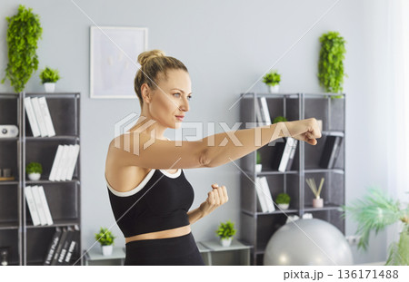 Woman performing boxing punches at home workout, side view in bright interior 136171488