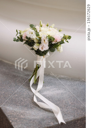 Wedding bouquet with white roses and pink lisianthus on stone windowsill near white wall 136172629