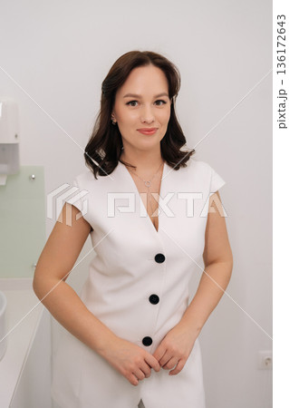 Portrait of skilled female cosmetologist smiling looking at camera, wearing uniform and conveying professionalism, expertise and caring patient-focused aesthetic medicine service in beauty clinic. 136172643