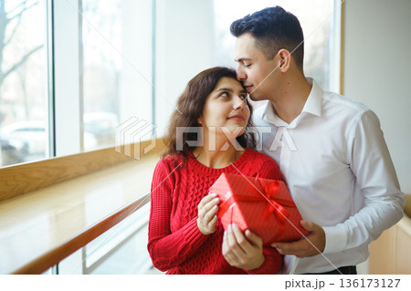 A young man gives his beloved a present and closes her eyes with a hand. Valentine's Day. 136173127