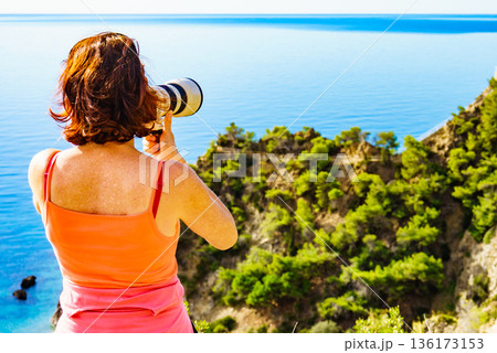 Woman with camera take travel photo on sea shore 136173153