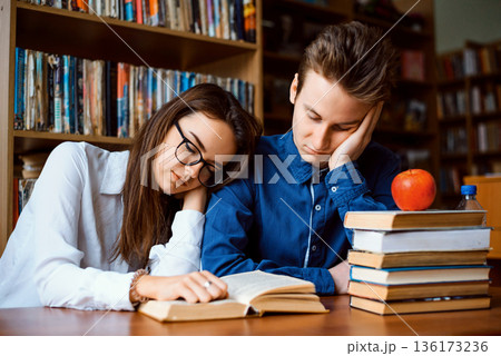 Two bored students in the library. Male and female students feeling sick and tired of preparation for final exams as they read many books lately 136173236