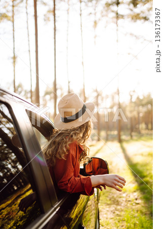 Young woman leaning out of the car window enjoying nature. Road trips summer holidays. 136173367