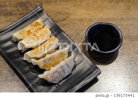 five pieces of gyoza in a black ceramic plate and sauce in a black ceramic cup on wooden floor background, food, snack, copy space five pieces of gyoza in a black ceramic plate and sauce in a black ceramic cup on wooden floor background, food, snack, copy space 136173441