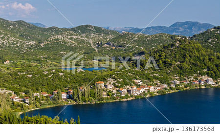 Aerial view of Dalmatian karst lake village in Croatia with waterfront houses green hills and calm water 136173568