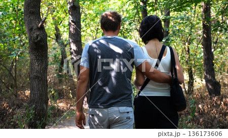 Happy couple walking along path at summer forest. Romantic pair going along trail at wild woodland. Lovers spending time together at nature. Concept of love and happiness. Slow motion Happy couple walking along path at summer forest. Romantic pair going along trail at wild woodland. Lovers spending time together at nature. Concept of love and happiness. Slow motion 136173606