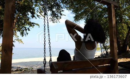 Happy woman ride on swing at tropical at sea beach. Carefree lady enjoying rest near ocean. Adult female having fun at sea shore on sunny day. Concept of summer vacation or holiday. Slow motion 136173607