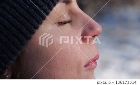 Detail view of attractive female face illuminating by warm rays of sun at winter day. Calm facial expression of young woman. Tranquil sight with green eyes of beautiful girl. Close up 136173614