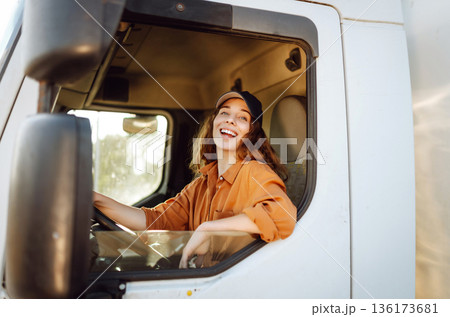 Portrait of beautiful young woman professional truck driver driving a big truck. Inside of vehicle 136173681