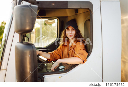 Portrait of beautiful young woman professional truck driver driving a big truck. Inside of vehicle Portrait of beautiful young woman professional truck driver driving a big truck. Inside of vehicle 136173682