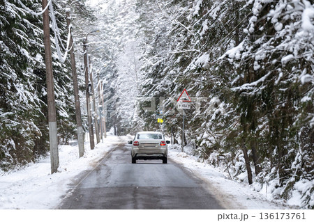 Car driving on frosty countryside road through spruce forest covered in snow on cold winter day. Car driving on frosty countryside road through spruce forest covered in snow on cold winter day. 136173761