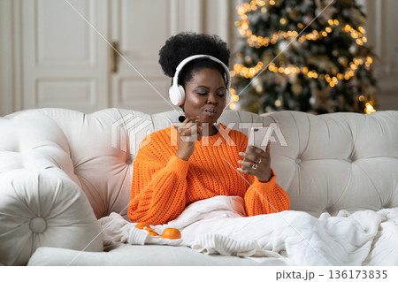 African woman spend christmas morning at home in living room with xmas tree read sms in smartphone African woman spend christmas morning at home in living room with xmas tree read sms in smartphone 136173835