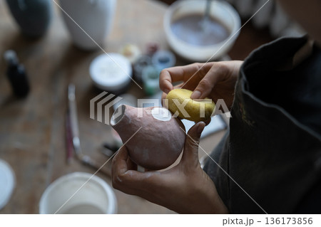 Young girl artisan busy with modelling jug vase from clay while pottery lesson or workshop in studio 136173856