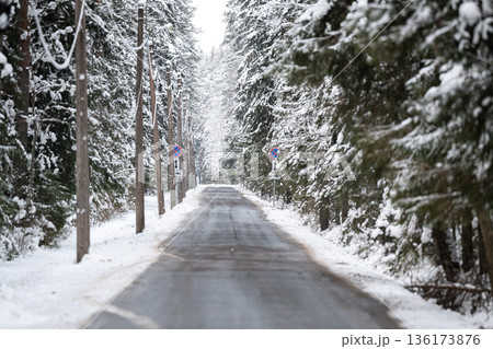 Countryside roadway with signs surrounded by spruce trees forest covered in snow on cold winter day. 136173876