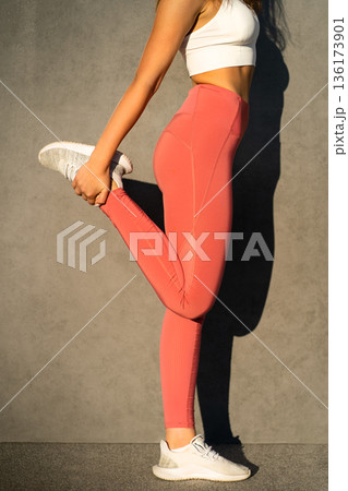 Sporty woman in pink sportswear stretch knee muscles, hold leg tightly back, unrecognizable closeup 136173901