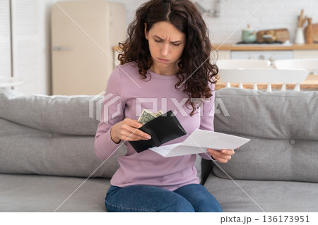 Sad young girl holding last cash money feeling anxiety about debt or bankruptcy, sitting at home. Sad young girl holding last cash money feeling anxiety about debt or bankruptcy, sitting at home. 136173951