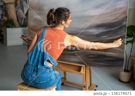 Concentrated female art hobby lover painting picture on canvas with oils at home studio workshop. 136174071