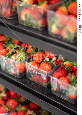 Fresh red strawberries packed in plastic containers and displayed in refrigerator unit for storage. 136174072