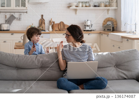 Freelancer mom working on laptop at home during lockdown, noisy child distracts asking attention. 136174087