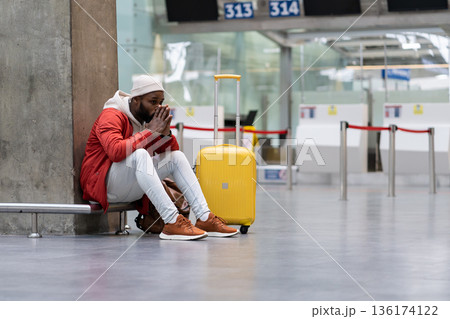 Exhausted African man on a long night connection at airport, waiting for a plane sitting in terminal 136174122