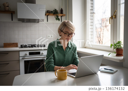Positive busy middle aged business woman typing on laptop, working on remote from home in morning. 136174132