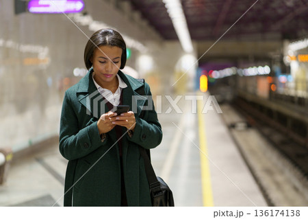 Serious businesswoman focused on business email in mobile phone waiting for train at underground Serious businesswoman focused on business email in mobile phone waiting for train at underground 136174138