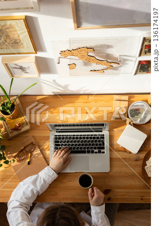 Wooden desktop top view, woman designer hands using laptop and holding a cup of coffee.Freelancer working place.Work from home. 136174197