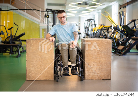 Focused disabled man athlete in wheelchair getting motivation in gym for long rehabilitation period. Focused disabled man athlete in wheelchair getting motivation in gym for long rehabilitation period. 136174244