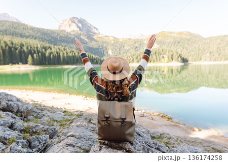 Back view young woman with backpack looking the view of the mountain lake in sunny weather. 136174258