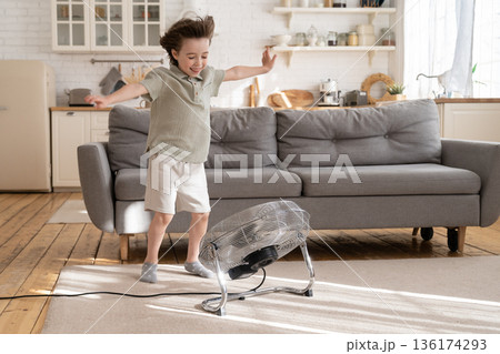 Small boy play with strong wind blow from ventilator or retro fan at home in cozy living room alone 136174293