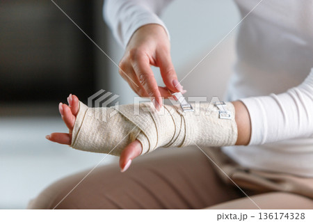 woman wrapping her painful wrist with elastic orthopedic bandage 136174328