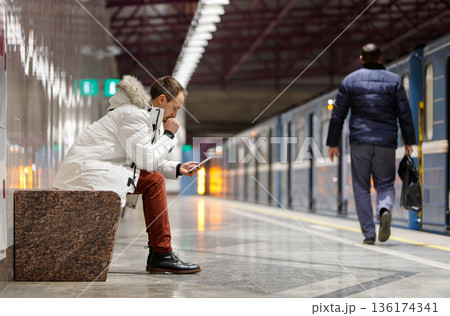 Thoughtful young man sit in subway, looking at smartphone, receiving message, reading news Thoughtful young man sit in subway, looking at smartphone, receiving message, reading news 136174341
