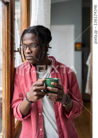 Depressed sad African guy holding cup of tea looking out window, having problems in personal life Depressed sad African guy holding cup of tea looking out window, having problems in personal life 136174346