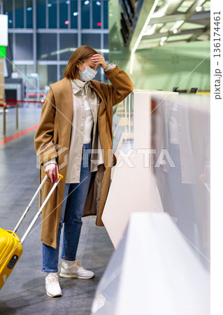 Woman with luggage upset over flight cancellation, stands at check-in counters at airport terminal 136174461