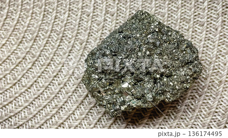 Raw pyrite crystal cluster with metallic shine on a neutral braided background for geology projects. 136174495
