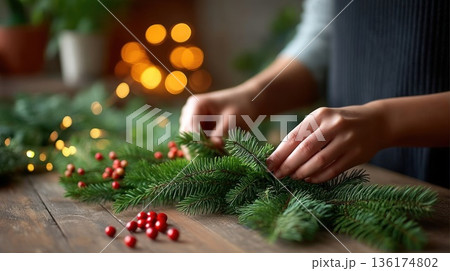 Hands crafting christmas garland with berries and lights on wooden table 136174802