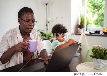 Black mother working from home with child drawing 136175078