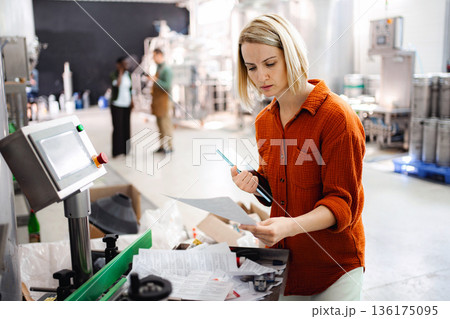 Woman inspecting paperwork and using tablet in brewery 136175095