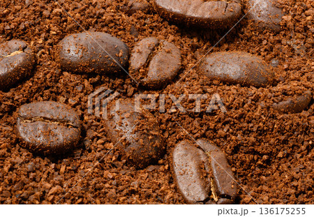 Whole roasted coffee beans lie on an even layer of freshly ground brown coffee. 136175255