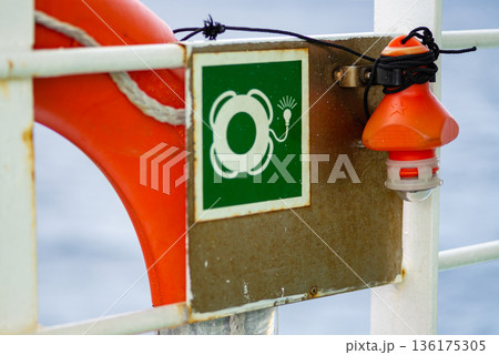 Emergency station sign and lifebuoy on ship wall highlighting maritime safety regulations and equipment. 136175305