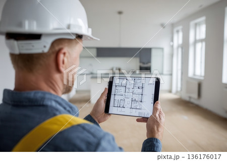 Construction worker reviewing blueprints on tablet in empty apartment Construction worker reviewing blueprints on tablet in empty apartment 136176017