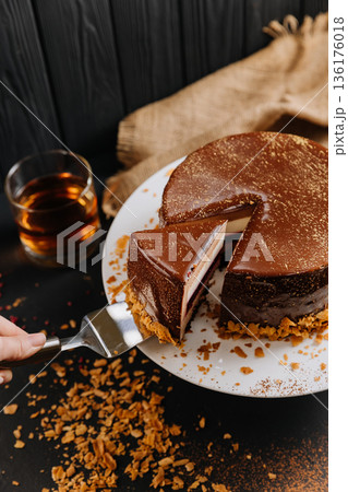 Layered chocolate mousse cake slice with raspberry jelly on spatula, dark background Layered chocolate mousse cake slice with raspberry jelly on spatula, dark background 136176018