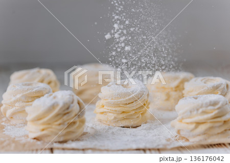 Powdered sugar falling on vanilla zephyr rosettes on parchment, rustic background 136176042