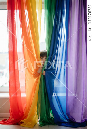 カラフルレインボーカラーのカーテンの後ろに隠れて顔を出す子供 カラフルレインボーカラーのカーテンの後ろに隠れて顔を出す子供 136176786